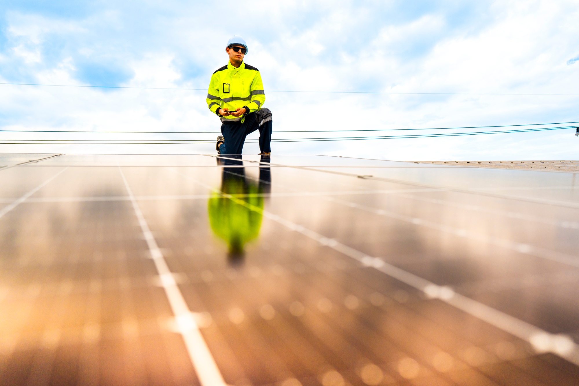 A technician in safety gear inspects solar panels on a metal rooftop